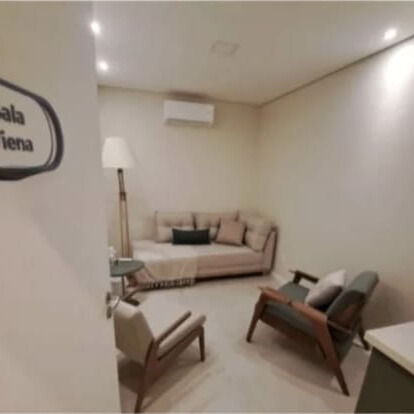 Sala de atendimento acolhedora com sofá bege em L,
                         duas poltronas de madeira e iluminação indireta.