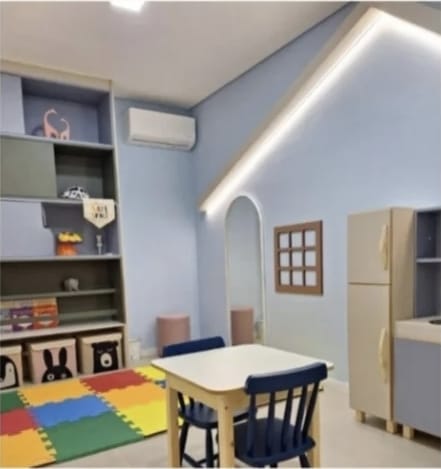 Espaço terapêutico infantil com tapete colorido, mesa infantil e prateleiras com brinquedos e livros.