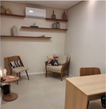 Consultório com poltronas de madeira, mesa de atendimento e prateleiras decorativas na parede.